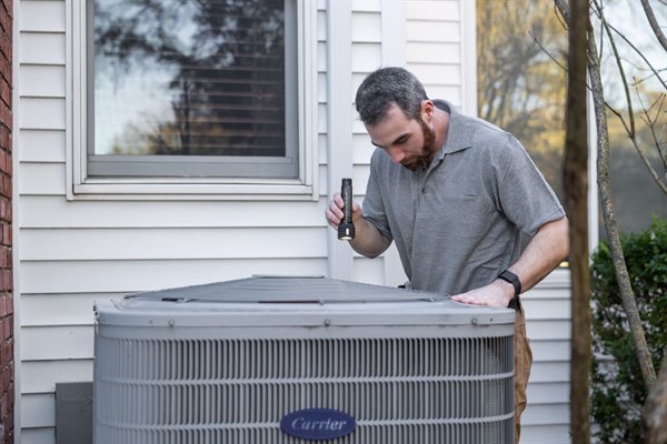 Technician inspecting an outdoor HVAC unit with gauges during a maintenance check