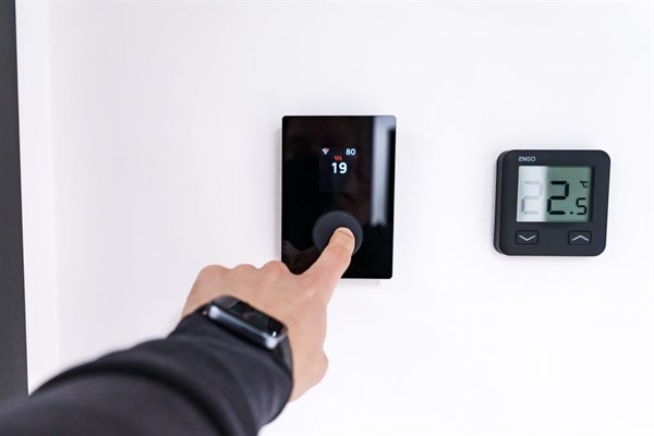 Hand adjusting a wall mounted thermostat to change the temperature setting